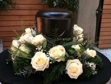 Schwarze Urne mit weißen Rosen auf floralem Trauerarrangement